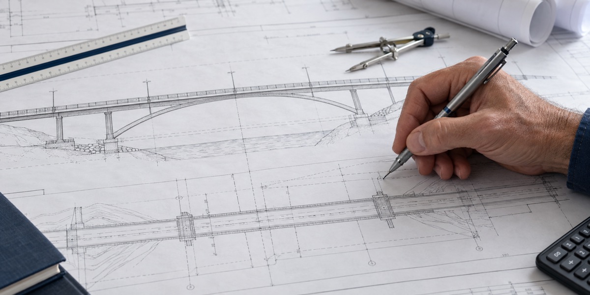 Engineer drawing a bridge elevation and plan by hand at a drafting table